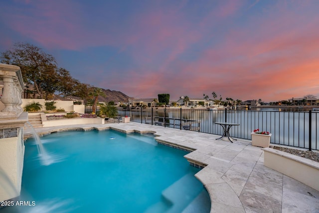 pool at dusk featuring a water view, pool water feature, and a patio