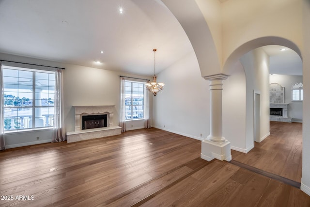 unfurnished living room with decorative columns, wood-type flooring, lofted ceiling, and a high end fireplace