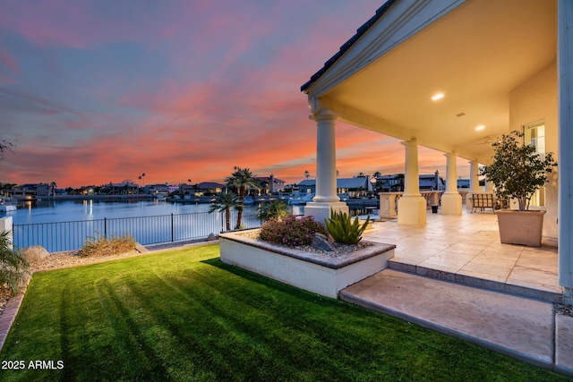 yard at dusk with a water view and a patio area