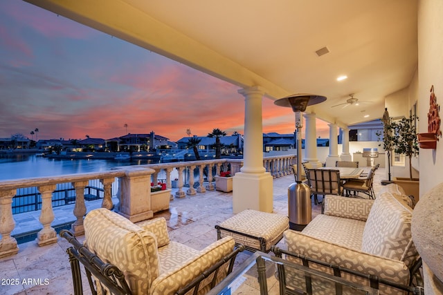 patio terrace at dusk featuring a water view, ceiling fan, and an outdoor living space