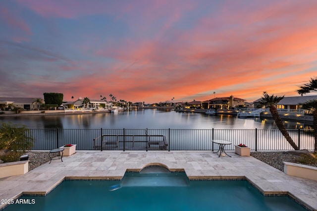 pool at dusk featuring a jacuzzi, a patio area, and a water view