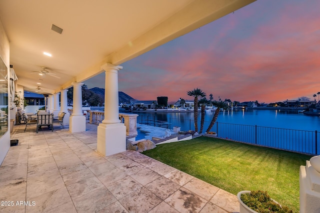 patio terrace at dusk featuring a water view, a yard, and ceiling fan