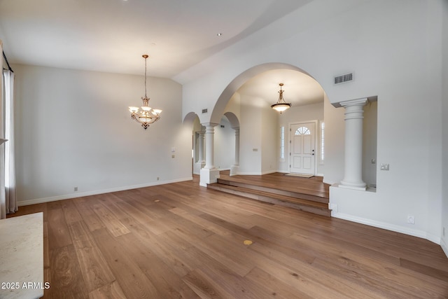 unfurnished living room with lofted ceiling, wood-type flooring, and ornate columns