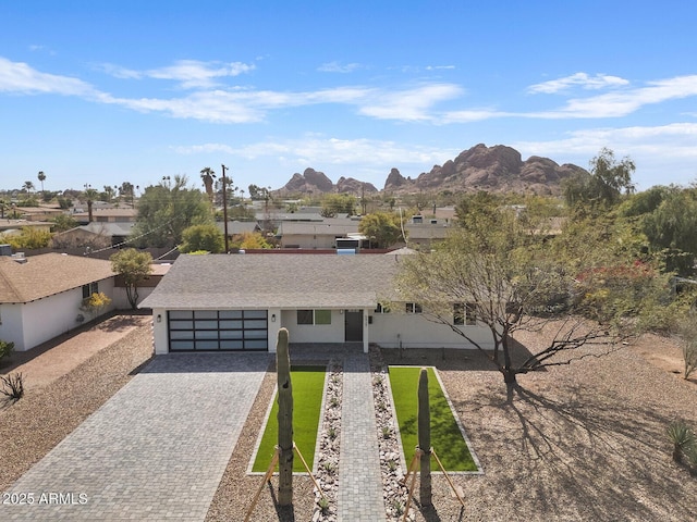 view of front facade featuring a garage, a shingled roof, decorative driveway, a mountain view, and stucco siding