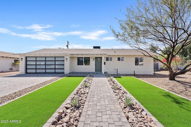 ranch-style house featuring a garage, a front yard, decorative driveway, and stucco siding