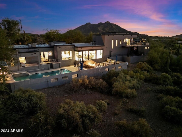 back house at dusk featuring a patio, a mountain view, and a fenced in pool