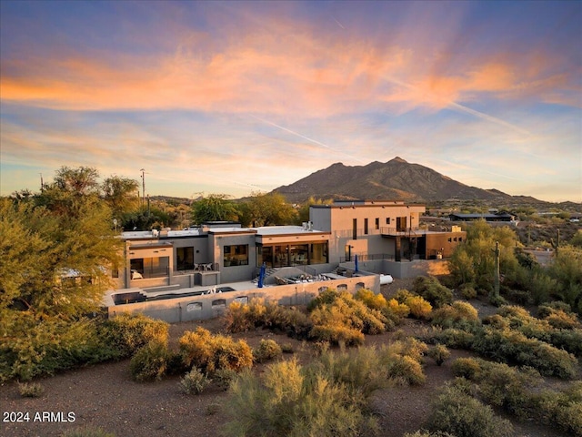 back house at dusk with a balcony, a mountain view, and a patio