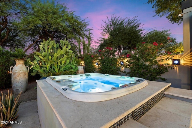 pool at dusk with an outdoor hot tub