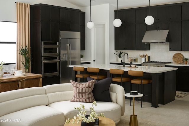 kitchen featuring appliances with stainless steel finishes, pendant lighting, a kitchen bar, decorative backsplash, and a center island with sink