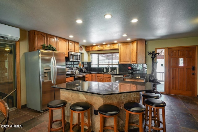 kitchen with a center island, a wall mounted air conditioner, appliances with stainless steel finishes, a kitchen bar, and sink