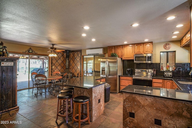 kitchen featuring ceiling fan, sink, an AC wall unit, stainless steel appliances, and a kitchen breakfast bar