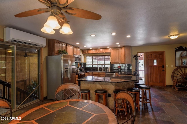 kitchen with a wall unit AC, ceiling fan, a breakfast bar, dark tile flooring, and stainless steel appliances