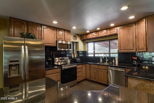 kitchen featuring dark tile floors, appliances with stainless steel finishes, dark stone countertops, and sink