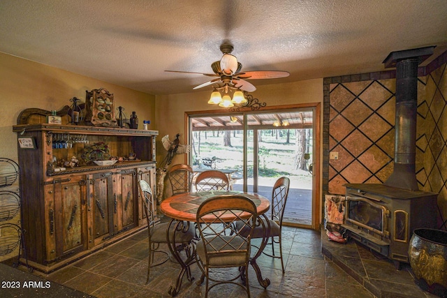 dining room featuring ceiling fan, a wood stove, dark tile flooring, and a textured ceiling