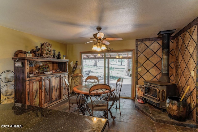 tiled dining area with a textured ceiling, a wood stove, and ceiling fan