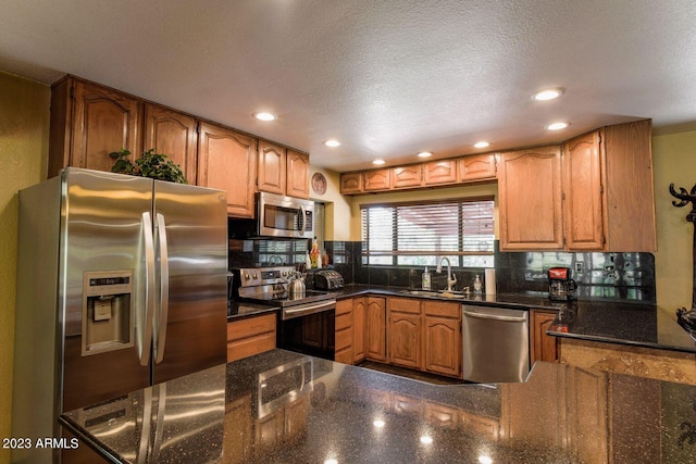 kitchen featuring appliances with stainless steel finishes, dark stone counters, a textured ceiling, and sink