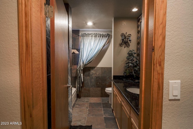 full bathroom featuring tile walls, vanity, tub / shower combination, toilet, and a textured ceiling