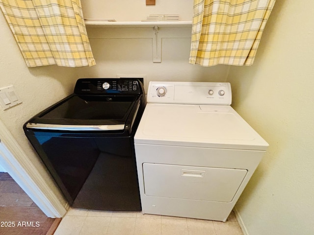 clothes washing area with washer and dryer, laundry area, light tile patterned floors, and baseboards