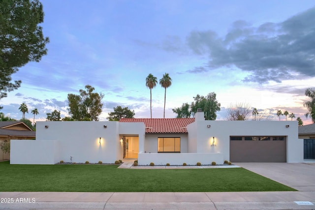 view of front of property featuring a garage, concrete driveway, a lawn, a tile roof, and stucco siding