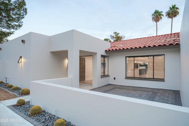 entrance to property featuring a patio area, a tiled roof, and stucco siding