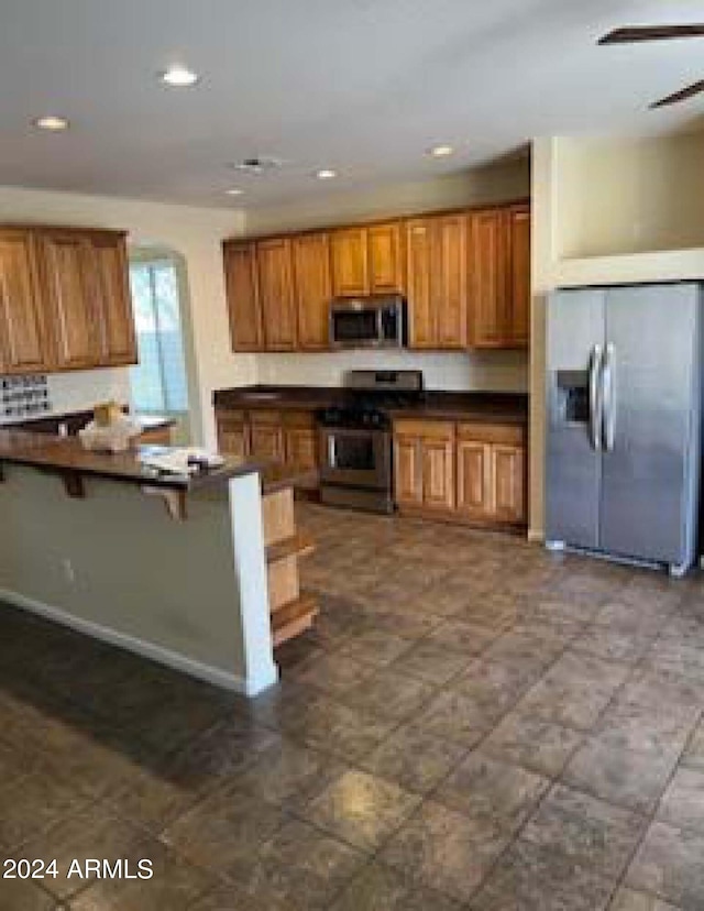 kitchen with appliances with stainless steel finishes, kitchen peninsula, ceiling fan, and a breakfast bar area