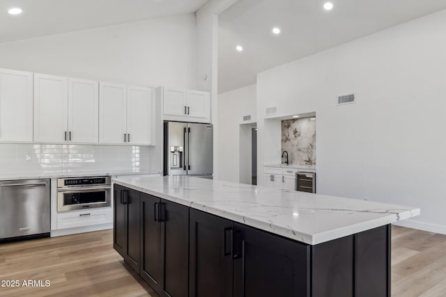 kitchen featuring high vaulted ceiling, white cabinets, decorative backsplash, appliances with stainless steel finishes, and light stone counters