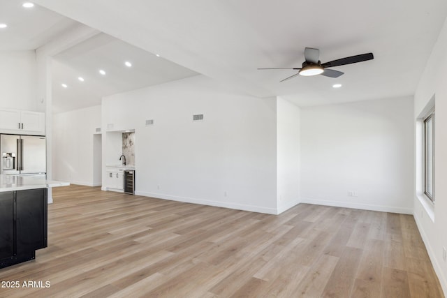 unfurnished living room with ceiling fan, beverage cooler, sink, high vaulted ceiling, and light hardwood / wood-style floors