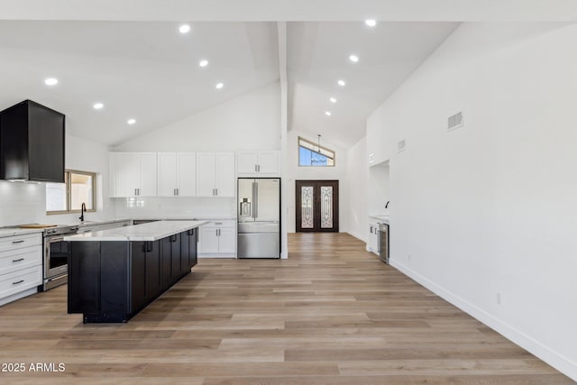 kitchen featuring appliances with stainless steel finishes, backsplash, high vaulted ceiling, a center island, and white cabinetry