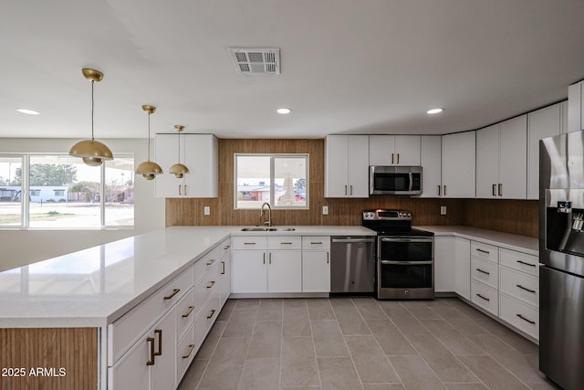 kitchen featuring sink, white cabinetry, hanging light fixtures, appliances with stainless steel finishes, and kitchen peninsula