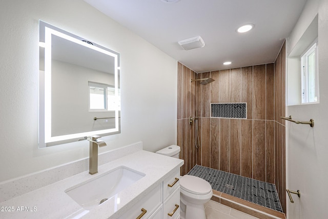 bathroom with a tile shower, vanity, and toilet