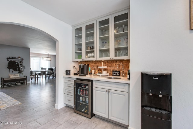 bar featuring backsplash, white cabinets, hanging light fixtures, sink, and wine cooler