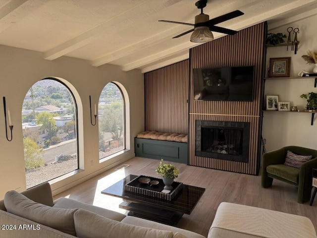 living room featuring ceiling fan, light hardwood / wood-style floors, a large fireplace, and beam ceiling