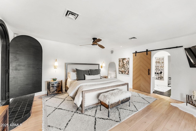 bedroom with ceiling fan, light hardwood / wood-style flooring, and a barn door