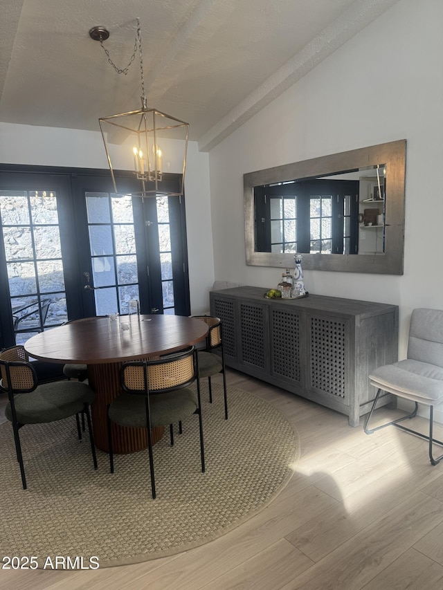 dining area with light wood-type flooring, a notable chandelier, french doors, and vaulted ceiling with beams