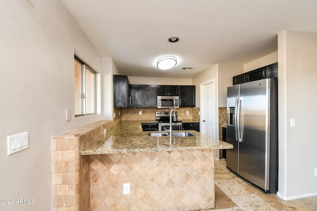 kitchen with light stone countertops, appliances with stainless steel finishes, sink, backsplash, and kitchen peninsula