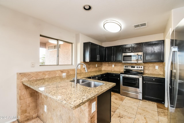 kitchen featuring light stone countertops, sink, kitchen peninsula, stainless steel appliances, and decorative backsplash