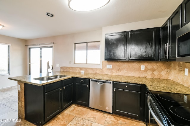 kitchen featuring kitchen peninsula, decorative backsplash, light stone counters, appliances with stainless steel finishes, and sink