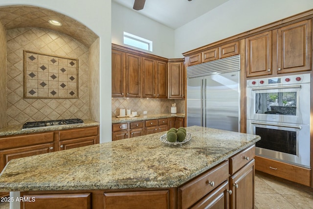 kitchen with light tile patterned flooring, a kitchen island, backsplash, stainless steel appliances, and light stone countertops