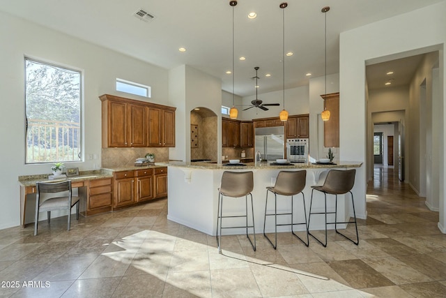 kitchen featuring a breakfast bar, pendant lighting, decorative backsplash, stainless steel appliances, and light stone countertops