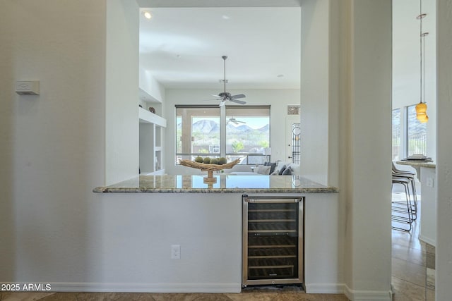 kitchen with pendant lighting, wine cooler, ceiling fan, light stone counters, and built in shelves