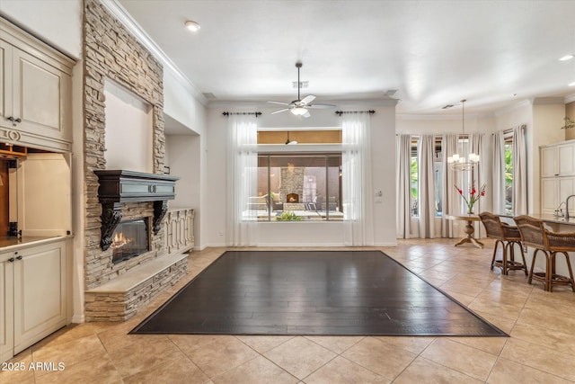 living room with light tile patterned floors, a stone fireplace, crown molding, and ceiling fan with notable chandelier