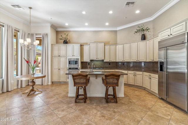 kitchen featuring built in appliances, a center island with sink, visible vents, and a sink