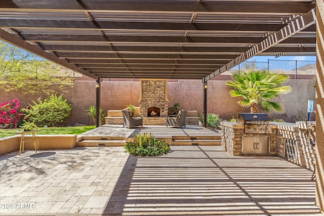 view of patio / terrace with grilling area, exterior kitchen, an outdoor stone fireplace, and a fenced backyard