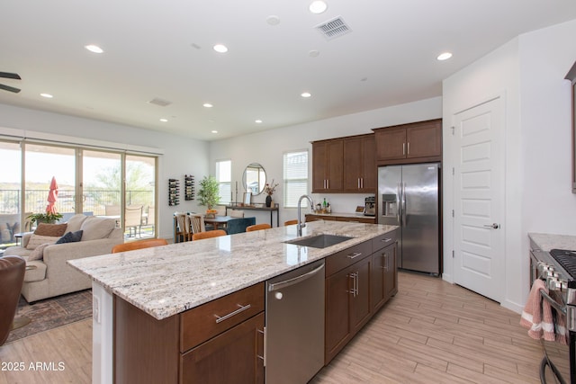 kitchen featuring light hardwood / wood-style flooring, appliances with stainless steel finishes, sink, light stone countertops, and a center island with sink