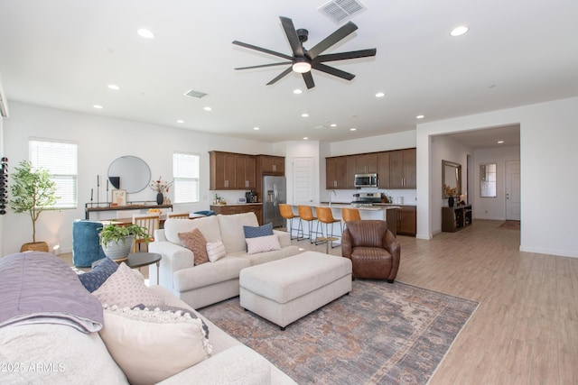 living room with sink, light wood-type flooring, and ceiling fan