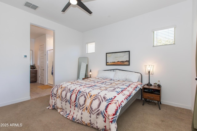 bedroom with ceiling fan, light colored carpet, ensuite bath, and multiple windows