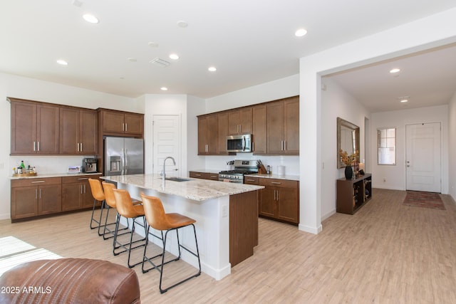 kitchen with appliances with stainless steel finishes, sink, light stone countertops, a breakfast bar, and an island with sink