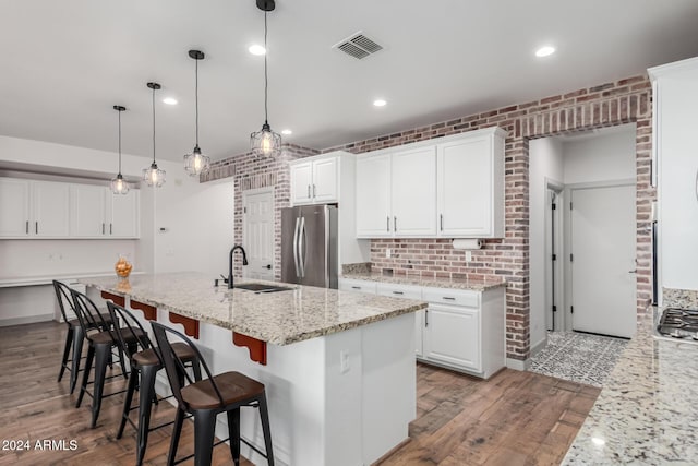 kitchen featuring white cabinets, stainless steel refrigerator, brick wall, and light stone counters