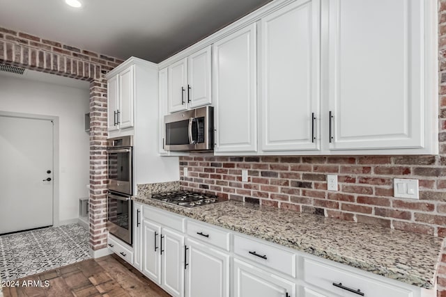 kitchen with white cabinets, appliances with stainless steel finishes, light stone countertops, and brick wall