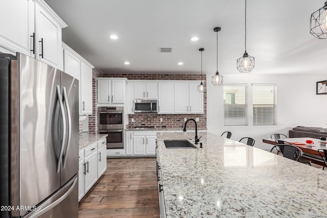 kitchen featuring light stone countertops, appliances with stainless steel finishes, sink, decorative light fixtures, and white cabinets